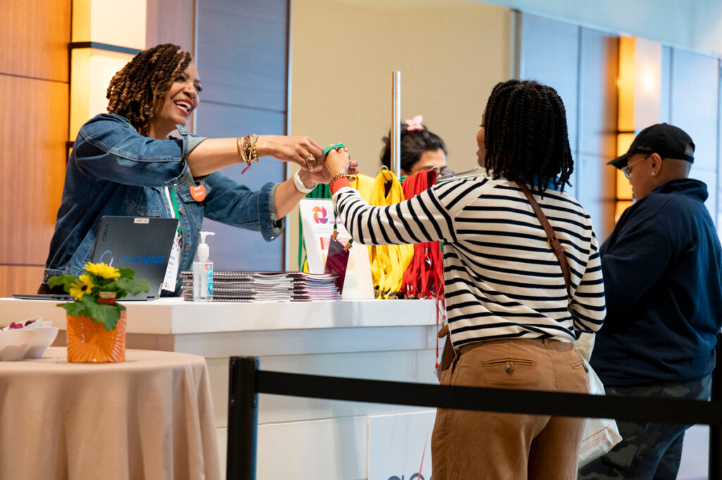 A GEO staff member smiles as she hands a conference lanyard to an attendee at the registration desk during a GEO conference while other attendees wait to check in.